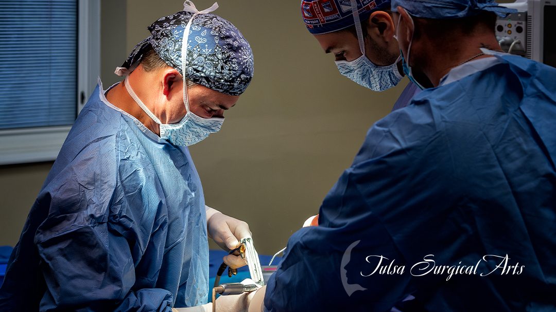 Dr. Angelo Cuzalina operating, in surgical cap and mask, with an assistant across the table